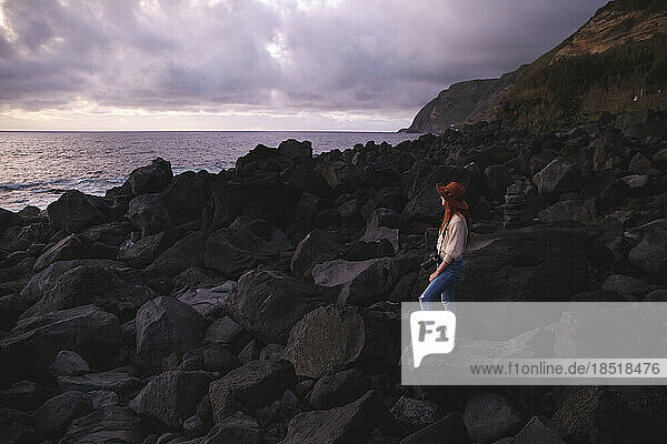 Woman wearing hat standing on rock at sunset