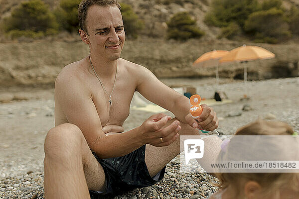 Father holding suntan lotion with daughter at beach