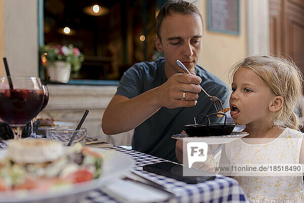 Man feeding shrimp to daughter in restaurant