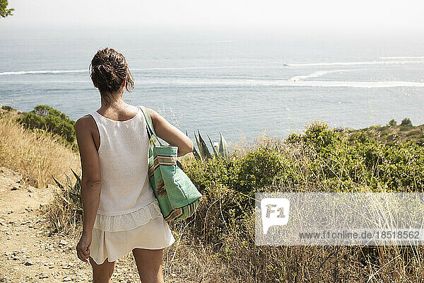 Frau mit Tasche geht an sonnigem Tag in Richtung Meer