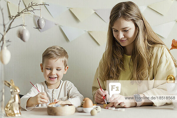 Smiling mother and son decorating Easter eggs at home