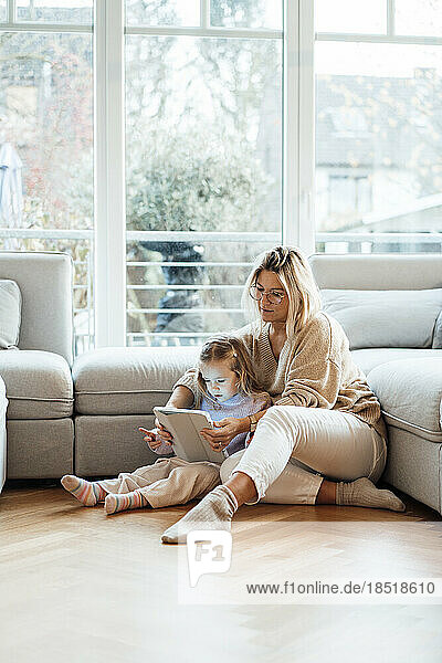 Woman sharing tablet PC with daughter sitting on floor in living room