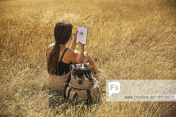 Young woman sitting on dry grass looking at flower drawing
