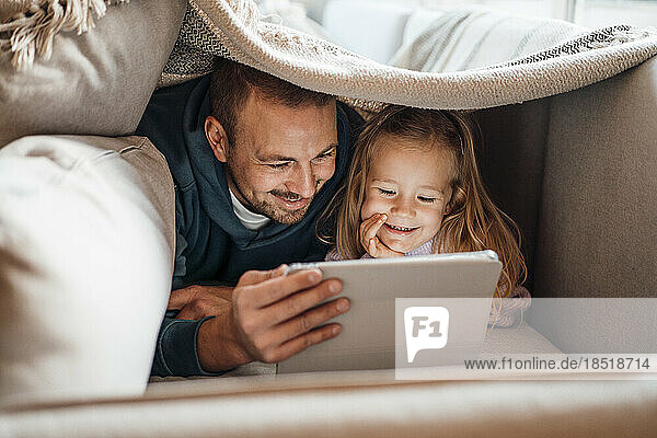 Happy father and daughter using tablet PC under blanket at home