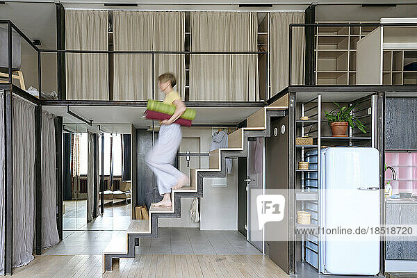 Woman carrying yoga mats descending stairs at home