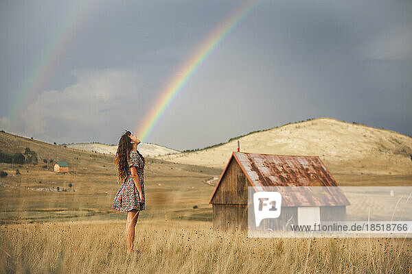 Young woman looking at rainbow standing in meadow