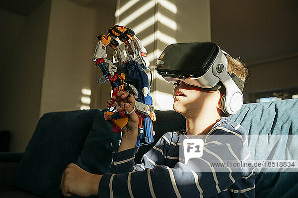 Boy wearing virtual reality simulator holding robotic arm at home