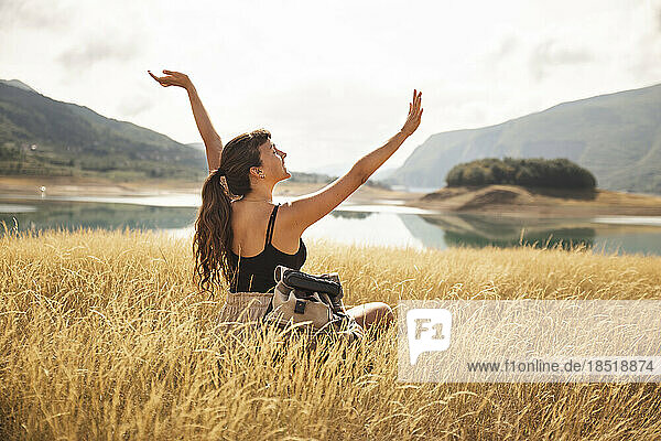 Carefree woman with arms raised sitting on dry grass