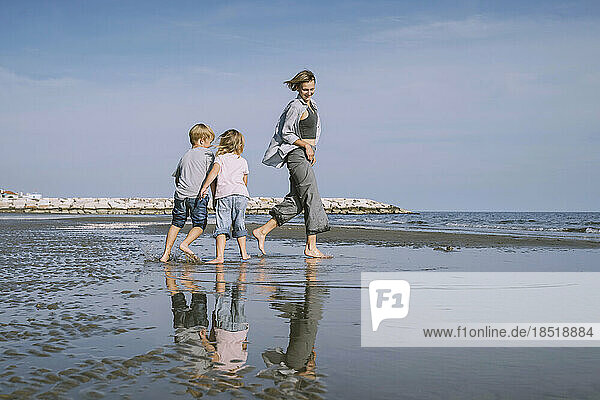 Happy mother playing with daughter and son on shore at beach