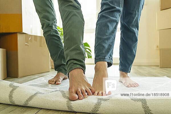 Couples unrolling carpet with legs in new home