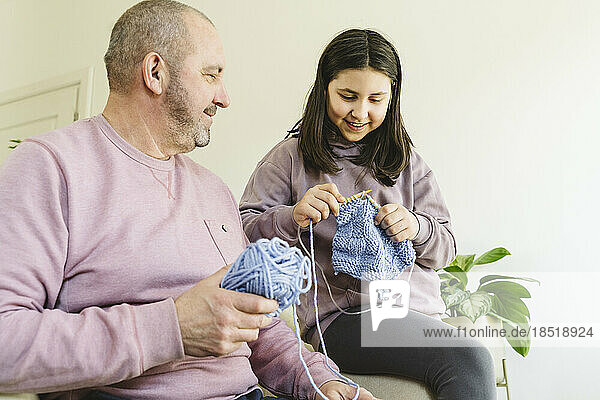 Grandfather and granddaughter knitting sweater at home