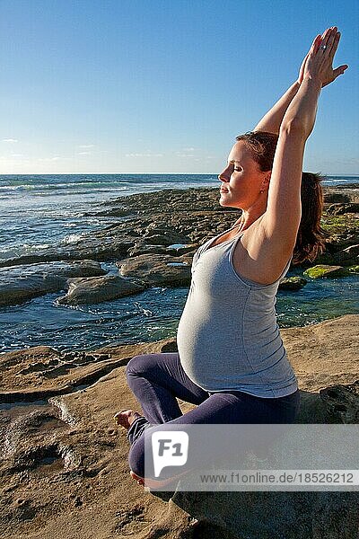 Schwangere Frau macht Yoga auf Felsen