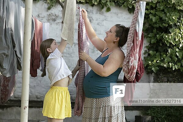 Kind hilft der schwangeren Mutter beim Wäsche aufhängen.  Bonn  Deutschland  Europa