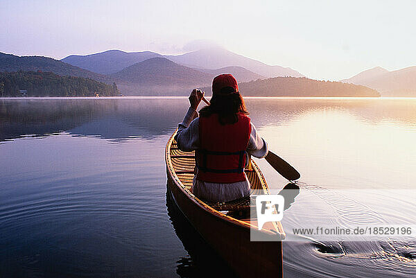 United States  New York  Rear view of woman paddling canoe on Lake Placid at sunrise  Adirondacks State Park