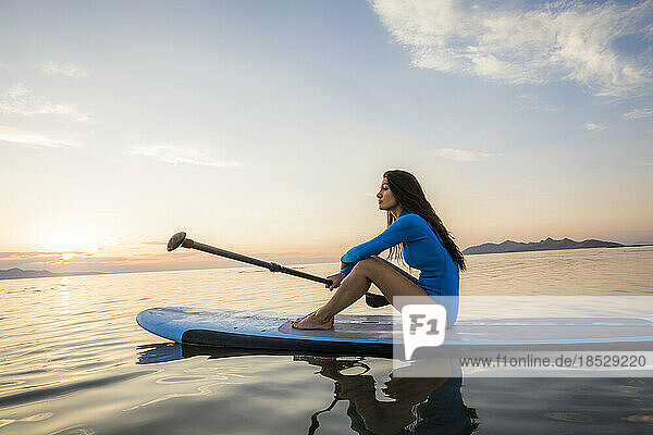 Woman sitting on paddleboard at sunset 