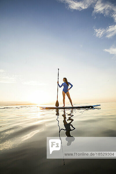 Woman standing on paddleboard at sunset 