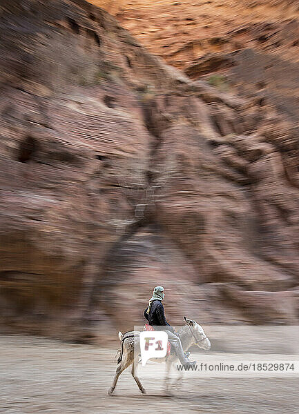 Mann reitet auf einem Esel umgeben von hohen Felsen in Petra; Petra  Jordanien