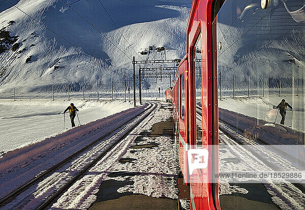 Cross country skier traverses a snowy trail near the train that passes through spectacular Alps scenery negotiating 55 tunnels and 196 bridges; Switzerland