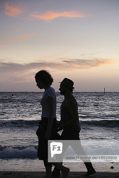 Silhouetted couple walking the beach at sunset; Melbourne  Victoria  Australia