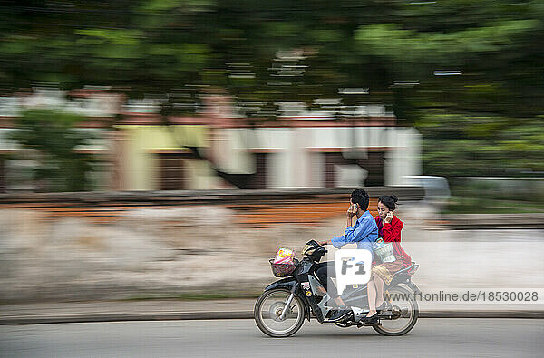 Motorcyclist and his rider both talking on a cell phone while underway; Luang Prabang  Laos
