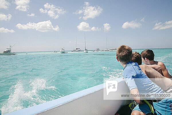 Drei Jungen blicken von einem Boot aus in Richtung Stingray City  einer beliebten vorgelagerten Sandbank  auf der sich die Rochen an den Menschen gewöhnt haben  so dass sie gefahrlos neben den Tieren schwimmen können; Grand Cayman  Cayman Islands