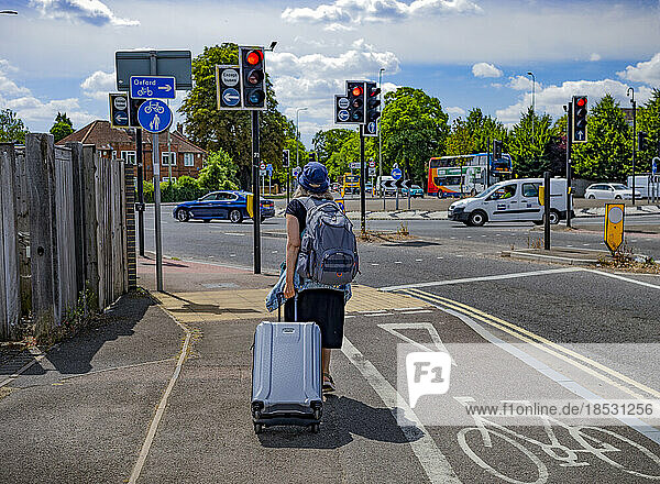 Frau  die einen Koffer auf einem Gehweg mit Blick auf den Verkehr in einem Kreisverkehr zieht; Oxford  England