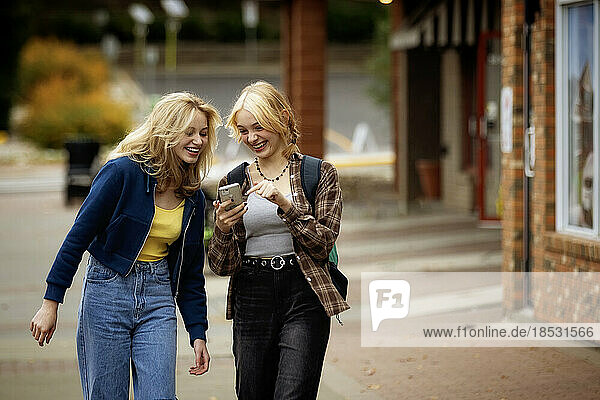 Two teenagers enjoying a day together shopping and walking down a street and using their smart phones on an autumn day; St. Albert  Alberta  Canada