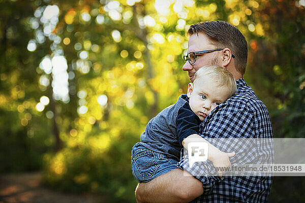 Father holds and comforts his baby boy outdoors in a park in autumn; Edmonton  Alberta  Canada