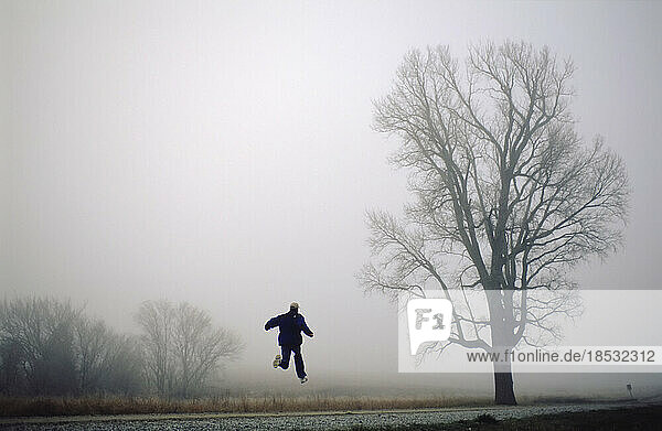 Junger Mann springt in die Luft in der Landschaft an einem nebligen Tag; Walton  Nebraska  Vereinigte Staaten von Amerika