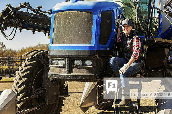 Porträt einer Landwirtin  die auf den Stufen eines Traktors mit Sämaschinenanbau sitzt; Alcomdale  Alberta  Kanada