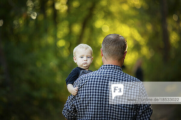 Vater geht mit seinem kleinen Jungen im Freien in einem Park spazieren  Blick auf den Rücken des Vaters  während das Baby in die Kamera schaut; Edmonton  Alberta  Kanada