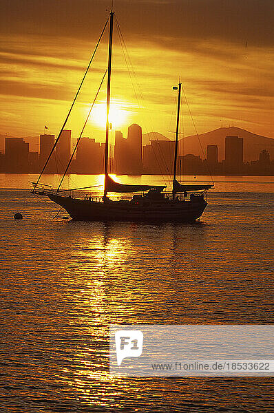 Silhouette eines Segelboots bei Sonnenaufgang mit der Skyline von San Diego in der Ferne  Kalifornien  USA; San Diego  Kalifornien  Vereinigte Staaten von Amerika
