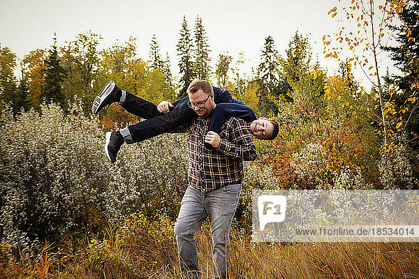 Father roughhousing with his son outdoors in a park area in autumn; Edmonton  Alberta  Canada