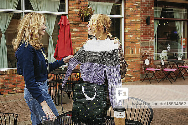 Zwei Teenager genießen die gemeinsame Zeit in einem Straßencafé  als ein Freund den anderen mit einem Pullover überrascht; St. Albert  Alberta  Kanada