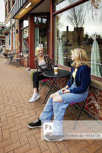 Zwei Teenager genießen die gemeinsame Zeit und sitzen an einem Kaffeetisch in einem Straßencafé; St. Albert  Alberta  Kanada