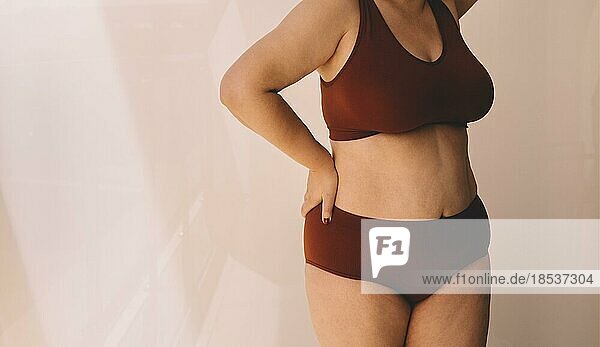 Female body in burgundy underwear. Woman embracing her natural body and curves against a light sunny background. Confident young woman feeling positive and comfortable in her body