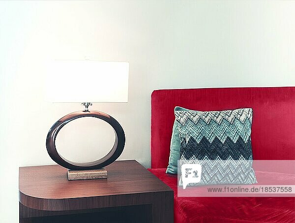 Eleganter Holztisch mit Lampe neben gemütlicher Couch mit Kissen in moderner Wohnung mit weißen Wänden platziert
