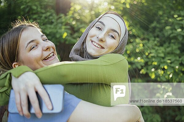 Starke weibliche Freundschaft. Glückliche zwei Teenagermädchen beste Freunde halten die Hände und umarmen  während sie vor einem Park stehen. Multiethnische Freunde