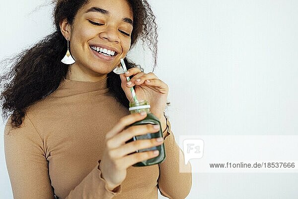 Fitness afro Frau hält ein Gemüse trinken. Junge Afroamerikanerin trinkt grünen Saft mit wiederverwendbarem Bambusstrohhalm in Loftwohnung. Home Konzept. Gesunder Lebensstil Konzept. Kopieren Raum