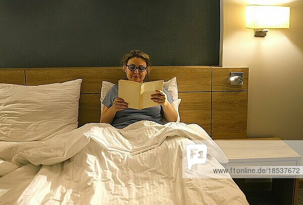 Mittleres Alter kaukasische Frau lesen Buch sitzen auf dem Bett im Schlafzimmer. Menschen  Schlafenszeit und Ruhe Konzept
