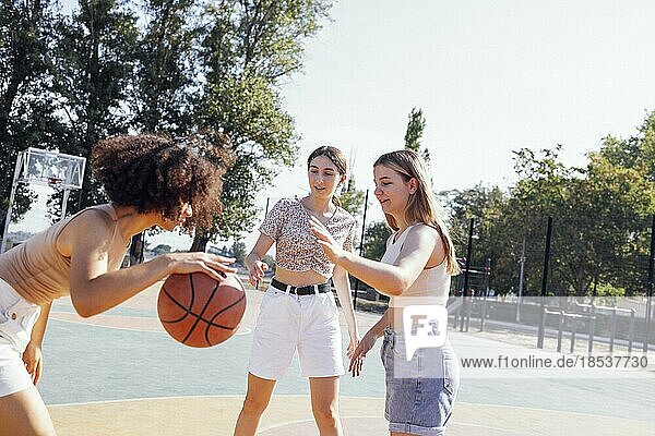 Multikulturelle Gruppe von jungen Freundinnen  die sich im Freien treffen und Spaß haben. Stilvolle coole Teenagermädchen versammeln sich am Basketballplatz  Freunde spielen Basketball im Freien