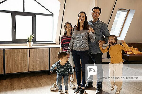Hauseigentum. Porträt der glücklichen jungen Familie  die den Schlüssel zeigt  der in der neuen Wohnung steht  ein fröhliches Paar mit Kindern  das sich nach dem Umzug in eine Wohnung umarmt. Versicherung  Immobilien  Hypothek Konzept