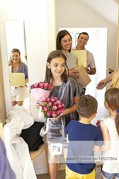 Happy smiling guests with presents standing in doorway. Focus on young female. Happy wedding day or anniversary. Pepple with joyful kids