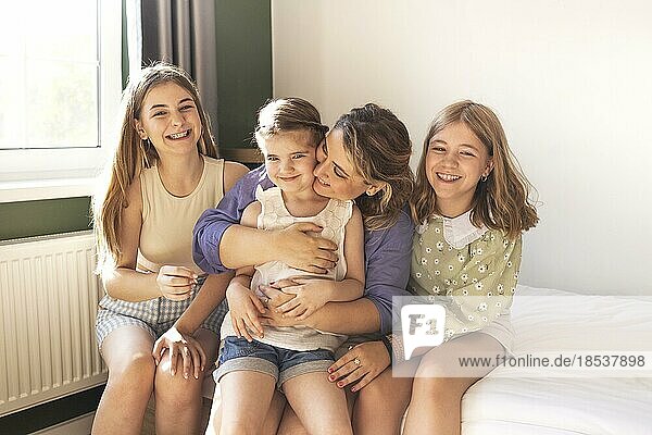 Glückliche drei Töchter und Mutter  die Spaß haben und Gespräche genießen  sitzen auf dem Sofa im modernen Wohnzimmer und lächeln. Mutter umarmt junge Töchter  kommunizierend