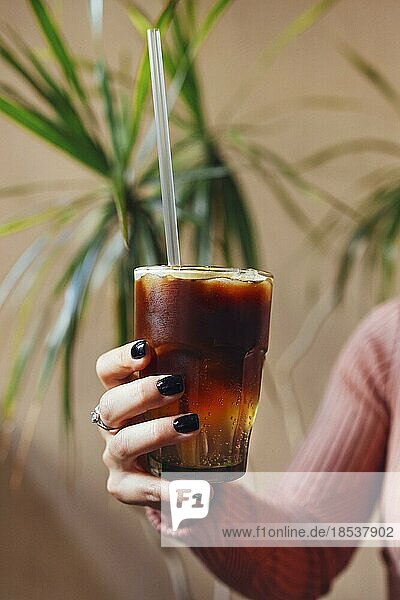 Iced coffee with orange in hand of the woman. Glass of americano mixed with craft soda and yuzu orange juice on blurred background  Refreshing summer drink concept