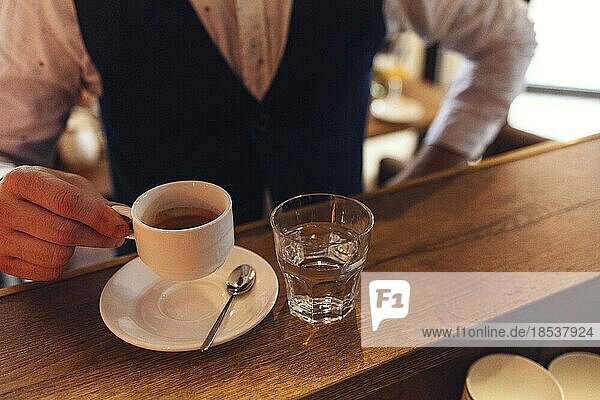 Männliche Hand hält weiße Tasse mit Espresso. Nahaufnahme mit selektivem Fokus. Blick auf Espresso bei einem Geschäftstreffen