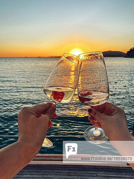 Weibliche Hände halten Gläser Champagner mit Himbeeren an Bord des Bootes. Sonnenuntergang Himmel und Meer auf dem Hintergrund. Machen Sie einen feierlichen Toast mit Sekt. Geburtstag  Urlaub  Party und Freundschaft Konzept