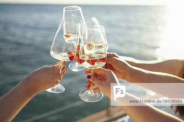 Weibliche Hände halten Gläser Champagner mit Himbeeren an Bord des Bootes. Sonnenuntergang Himmel und Meer auf dem Hintergrund. Machen Sie einen feierlichen Toast mit Sekt. Geburtstag  Urlaub  Party und Freundschaft Konzept