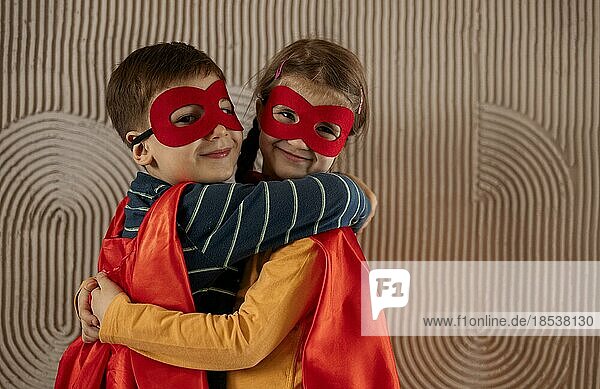 Porträt eines Teams von zwei jungen Superhelden  Bruder und Schwester  auf beigem Hintergrund. Superhelden Kind. Superheld Kind spielt zu Hause. Idee  Freiheit  Freundschaft  glückliches Kindheitskonzept
