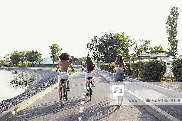 Teenager verschiedener Nationalitäten und unterschiedlichen Aussehens fahren auf Fahrrädern eine Stadtstraße entlang. Junge und positive Mädchen lächeln zusammen. Gesunder Lebensstil und Freundschaft Konzept